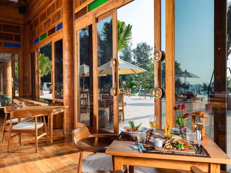 Licht restaurant met houten details en grote ramen met uitzicht op het zwembad en de tuin.