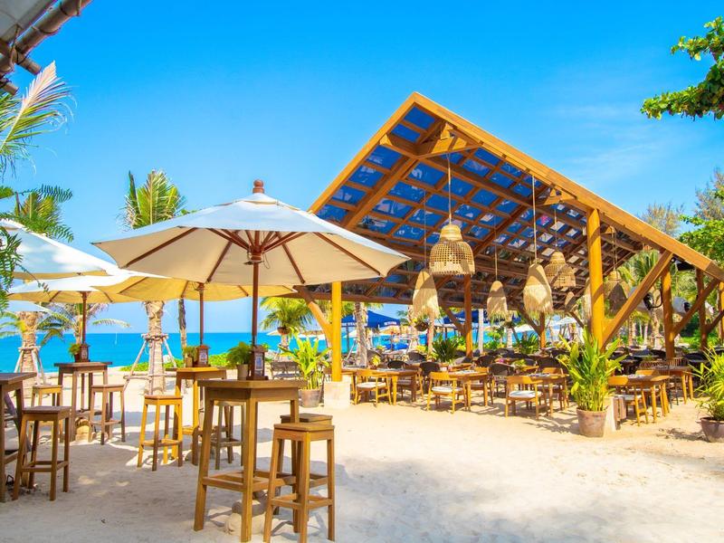 Strandrestaurant met houten stoelen, parasols en zeezicht op een zonnige dag.
