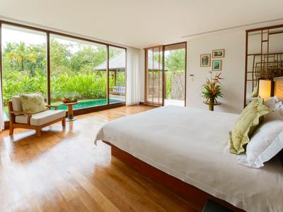 Jasna sypialnia z dużym łóżkiem, drewnianą podłogą i widokiem na ogród i basen przez okna sięgające od podłogi do sufitu.