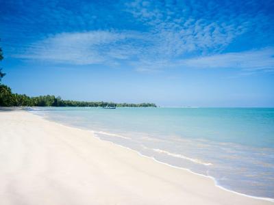 Pláž s bílým pískem a průzračnou modrou vodou pod jasnou oblohou.