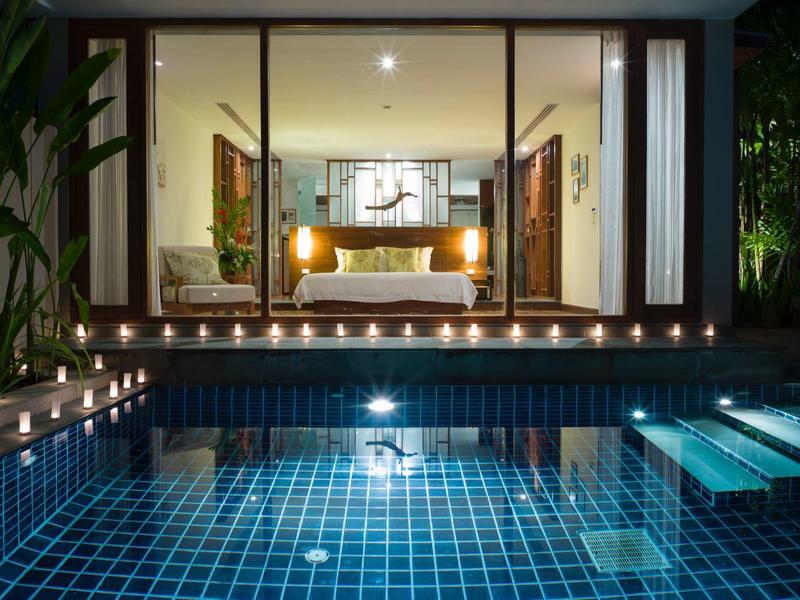 Nowoczesny pokój hotelowy z oświetlonym basenem przed tarasem nocą.