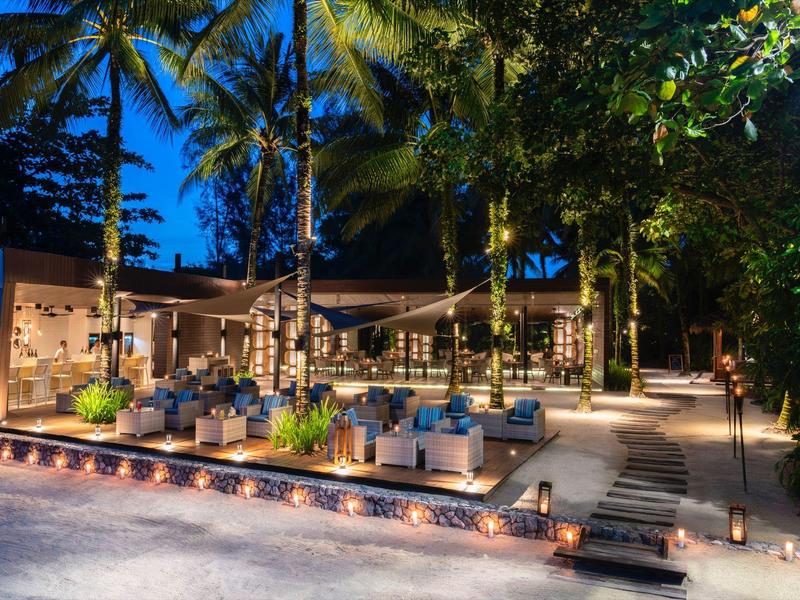 Przytulny zewnętrzny teren hotelu z miejscami do siedzenia i palmami nocą.