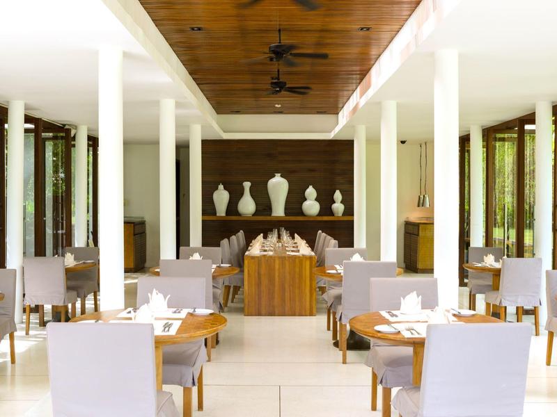 Jasna restauracja hotelowa z białymi krzesłami, drewnianymi stołami i dekoracyjnymi wazami na ścianie.