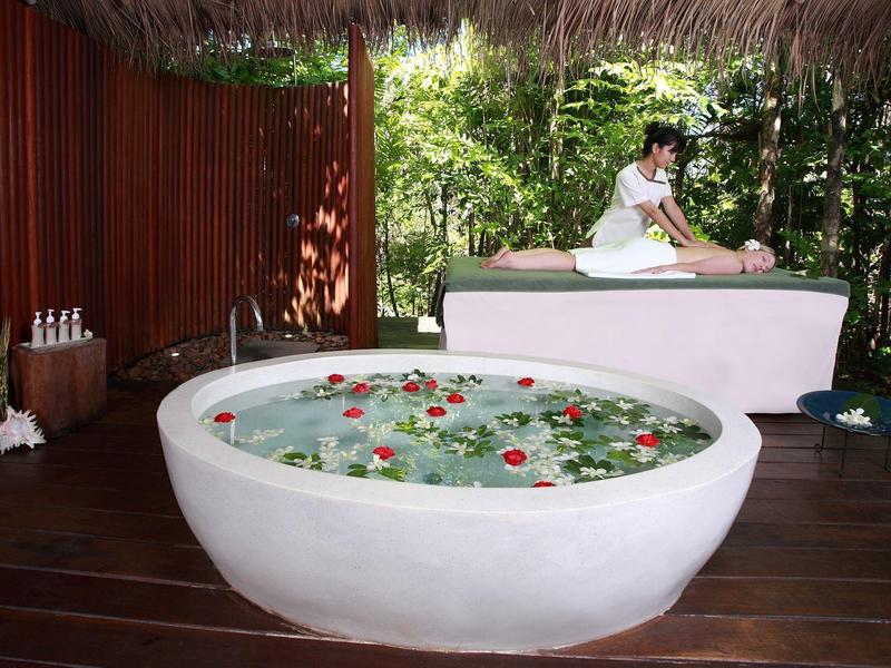 Strefa relaksu z dużą miską kwiatów i kobietą otrzymującą masaż.