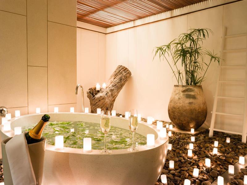 Strefa wellness z okrągłym jacuzzi, roślinami i wieloma świecami w spokojnym pomieszczeniu.