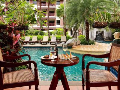 Zwei Stühle und ein Tisch mit Drinks am Pool vor tropischem Hintergrund in einem Hotel.