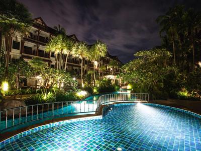 Beleuchteter Hotelpool in tropischer Umgebung bei Nacht mit Palmen und Vegetation.