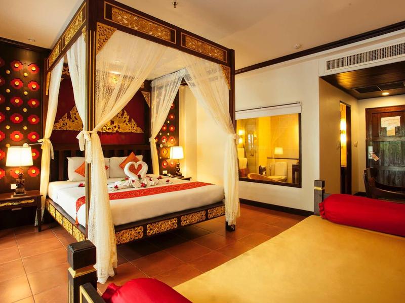 Elegantes Schlafzimmer mit Himmelbett, roten Dekokissen und warmem Licht in Holzmöbeln.