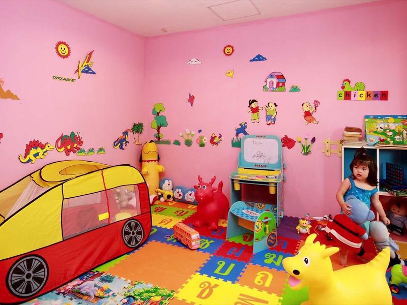Buntes Kinderspielzimmer mit rosa Wänden, Spielzeugauto, Matten und diversen bunten Spielsachen.