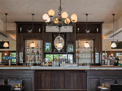 Bar elegante in hotel con legno scuro, lampade e grande orologio a parete.