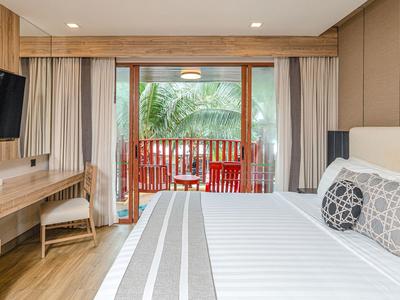 Nowoczesny pokój hotelowy z podwójnym łóżkiem, biurkiem, telewizorem i widokiem na taras z roślinnością tropikalną.