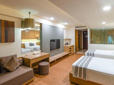 Camera d'hotel moderna con due letti, divano, scrivania e accenti in legno caldo.