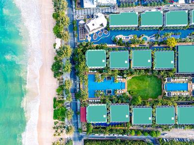 Vista aerea di un hotel con più tetti verdi accanto a una spiaggia sabbiosa e mare blu