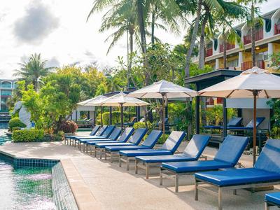 Rząd niebieskich leżaków obok basenu z parasolami i palmami w tle.