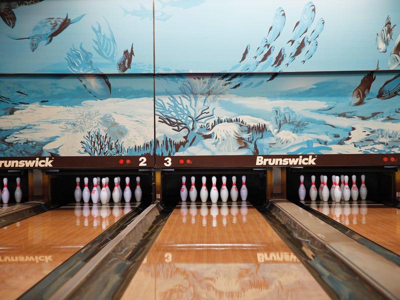 Due piste da bowling con birilli bianchi davanti a un muro con un murale subacqueo