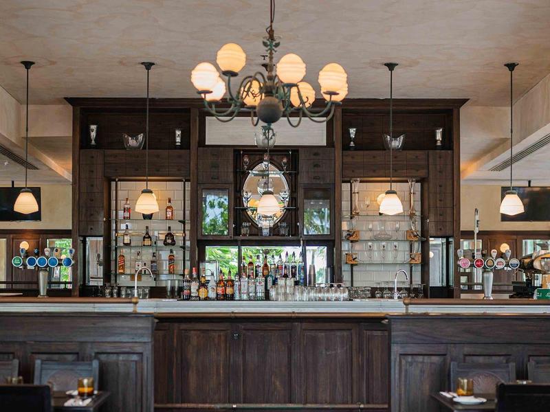 Bar elegante in hotel con legno scuro, lampade e grande orologio a parete.