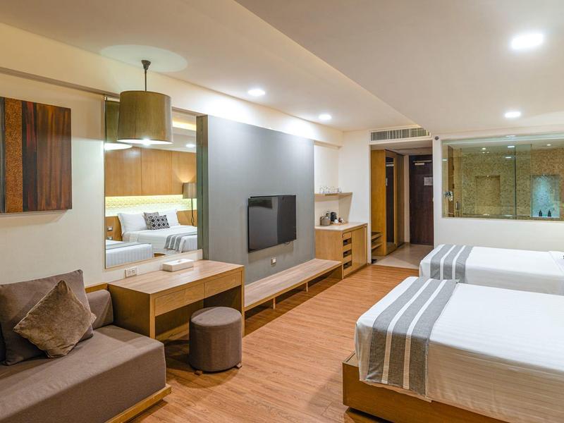 Camera d'hotel moderna con due letti, divano, scrivania e accenti in legno caldo.