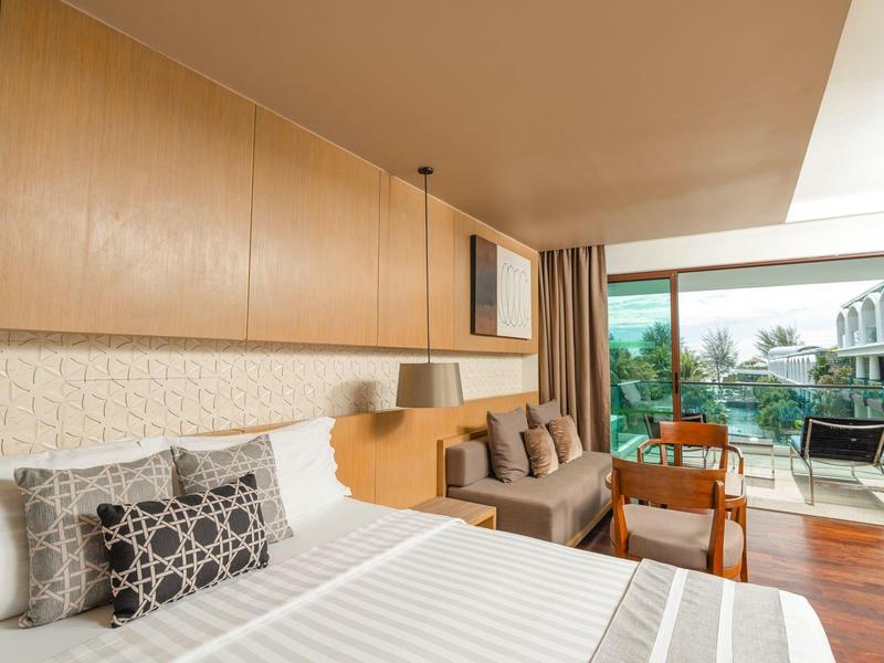 Camera d'hotel moderna con letto grande, divano e vista su terrazza e piscina.