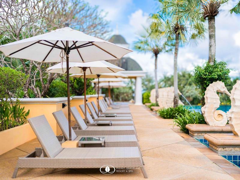 Area piscina interna con lettini, ombrelloni e piante tropicali in una giornata di sole.