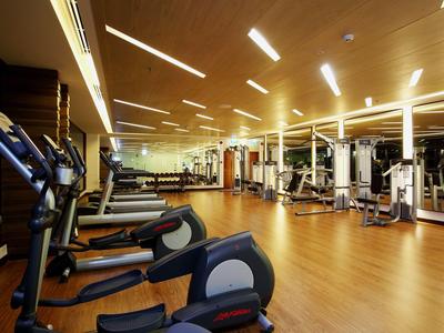 Grande salle de sport avec sol en bois, équipements modernes et éclairage de plafond lumineux.
