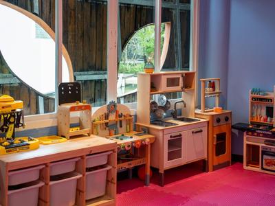 Dětská herní kuchyňka s hračkami před velkými okny a červeným kobercem.