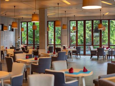 Moderní restaurace s velkými okny, kulatými stolem a čalouněnými židlemi za teplého osvětlení.