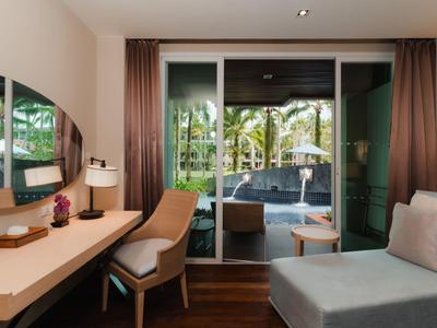 Moderní hotelový pokoj s psacím stolem, židlí, pohovkou a přístupem na balkon s výhledem na bazén.