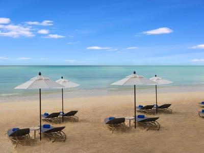 Písčitá pláž s lehátky a slunečníky u klidného moře pod modrou oblohou