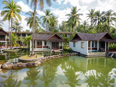 Bungalows sur l'eau avec des palmiers et un ciel nuageux en arrière-plan.