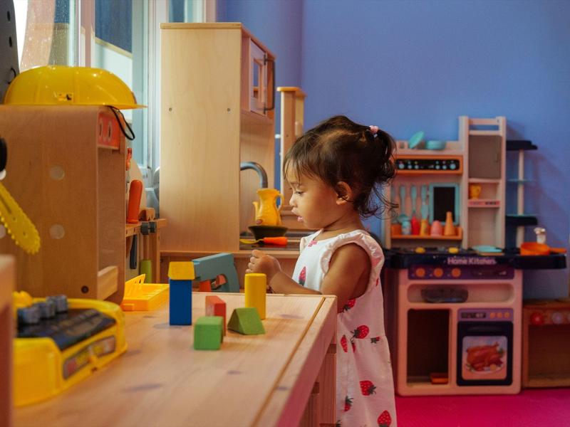 Malá dívka si hraje s barevnými dřevěnými kostkami na dřevěném stole v herně.