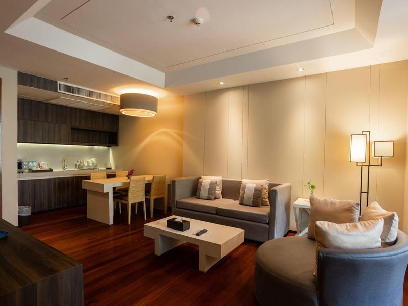 Moderní obývací pokoj s pohovkou, křesly, konferenčním stolkem a přilehlou kuchyní s jídelním koutem.