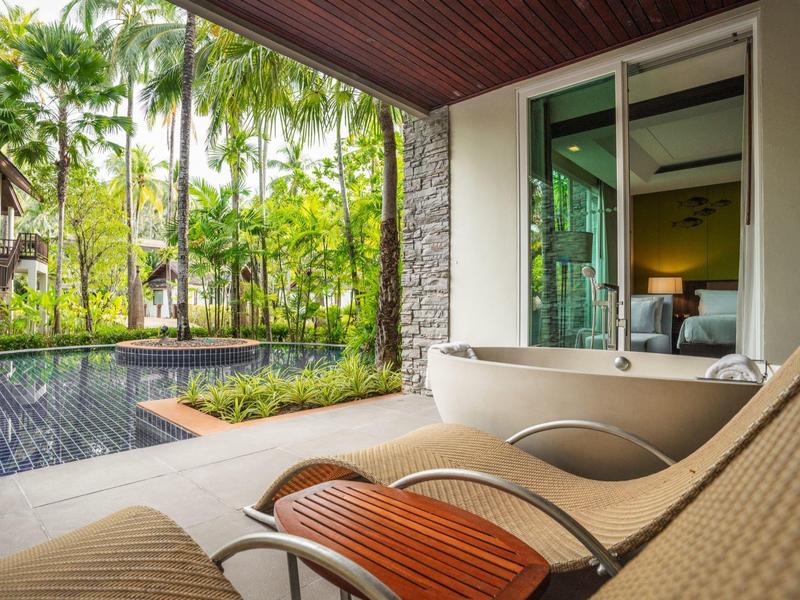 Dvě lehátka s výhledem na bazén a palmy v hotelovém prostředí.