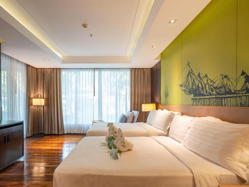 Moderní hotelový pokoj se dvěma queen postelemi, velkým oknem a světlým zeleným zdí s dekorací.