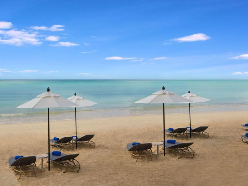 Písčitá pláž s lehátky a slunečníky u klidného moře pod modrou oblohou