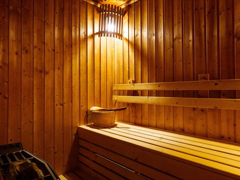 Dřevěná sauna s lavicemi, vědrem a naběračkou pod teplým osvětlením.