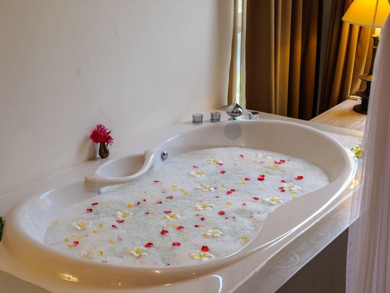 Bílá vana naplněná vodou s rozptýlenými červenými a bílými okvětními lístky