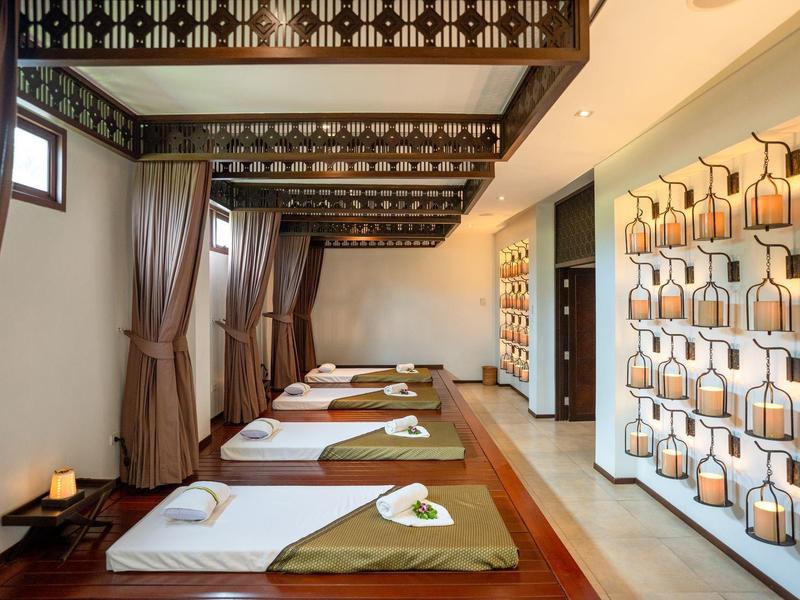 Světelná wellness masážní místnost s lehátky, závěsy a dekorativními nástěnnými lampami.