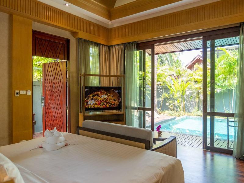 Hotelový pokoj s velkou postelí, televizí, posuvnými dveřmi a výhledem na bazén a zahradu.