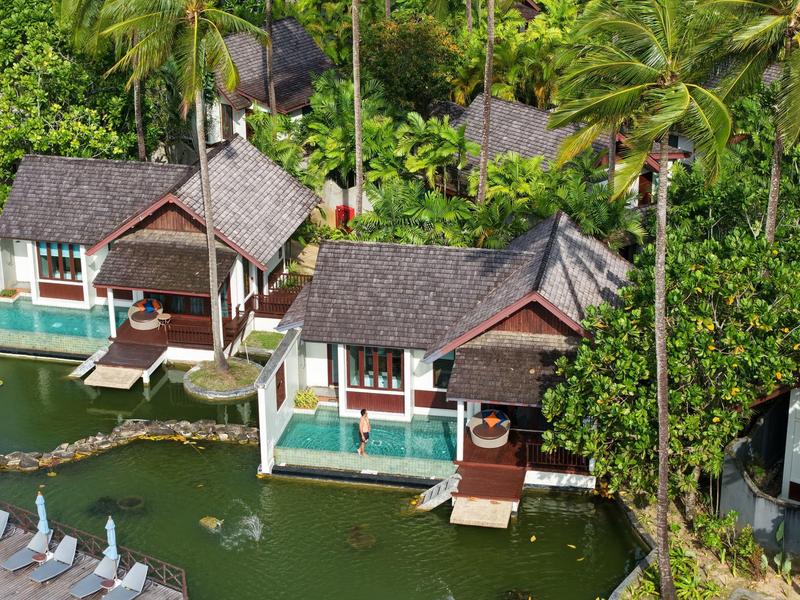 Přestavěné bungalovy s doškovými střechami obklopené palmami a zelenou vodou.
