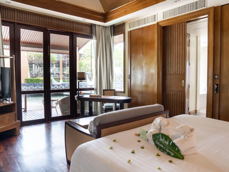 Světý hotelový pokoj s manželskou postelí, terasovými dveřmi a výhledem na bazén.