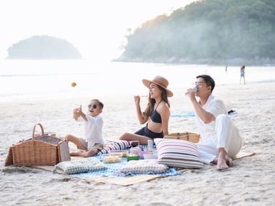 Famiglia seduta su una coperta che si gode un picnic sulla spiaggia con vista sul mare.