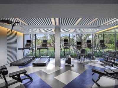 Palestra moderna con tapis roulant e pesi, grandi finestre con vista sul verde.