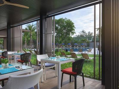 Offenes Restaurant mit Tischen, Stühlen und Blick auf einen Pool und grüne Bäume im Freien.