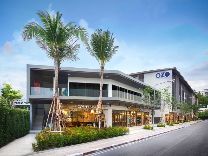 Modernes zweistöckiges Einkaufszentrum mit großen Glasfenstern, Palmen und breitem Gehweg.