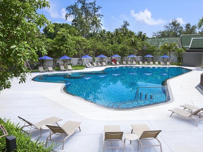 Großer Außenpool mit Liegestühlen und blauen Sonnenschirmen in einer gepflegten Gartenanlage.