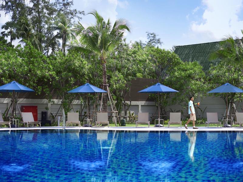 Blauer Pool mit Sonnenschirmen und grünen Palmen im Hintergrund unter blauem Himmel.