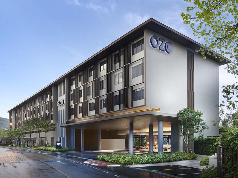 Modernes dreistöckiges Hotelgebäude mit großem Vordach und Glasfenstern, umgeben von Bäumen.