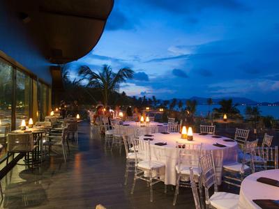 Restaurantterrasse mit gedeckten Tischen, brennenden Kerzen und Palmen bei blauem Abendhimmel.