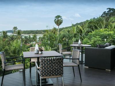 Terrassenbereich mit schwarzem Tisch und Stühlen, umgeben von üppigem grünem Tropenwald bei klarem Himmel.