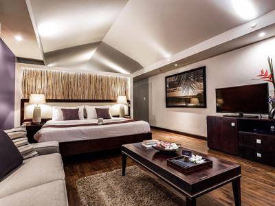 Modern hotelkamer met groot bed, bank, tv en decoratieve tafel onder warme verlichting.